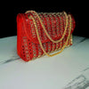 A red evening clutch bag adorned with red rhinestones and a gold diamond chain.