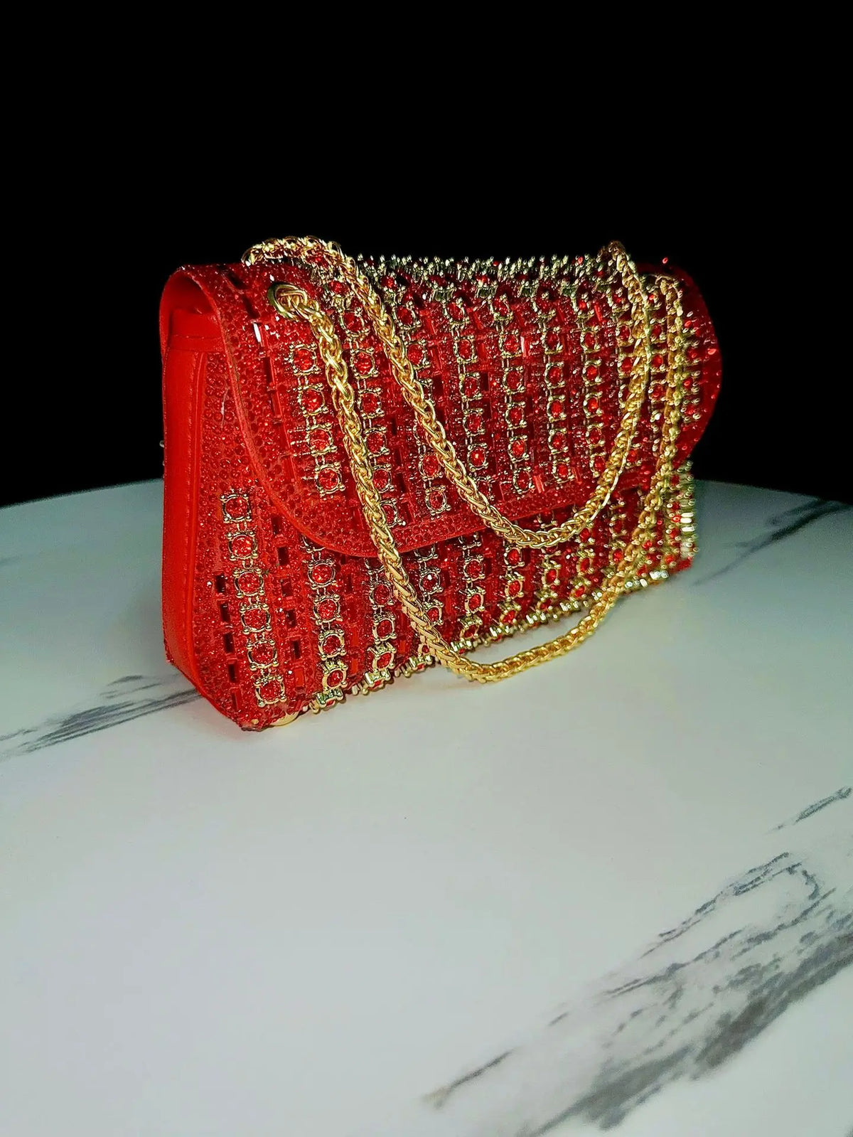 A red evening clutch bag adorned with red rhinestones and a gold diamond chain.