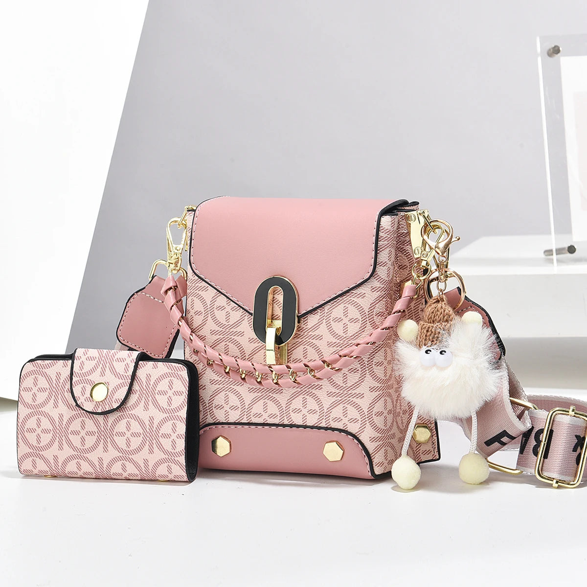 Sac bandoulière imitation cuir rose avec quincaillerie dorée et un charme blanc duveteux, exposé sur une surface blanche.