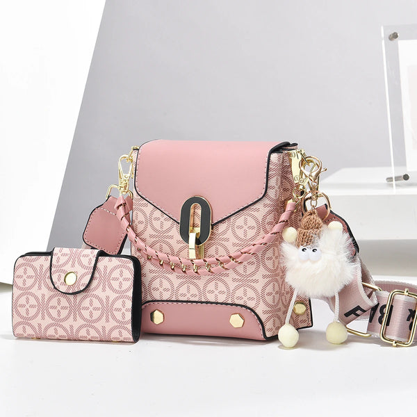 A pink faux leather crossbody bag with gold hardware and a fluffy white charm is displayed on a white surface.