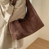 A close-up of a person wearing a beige shirt and carrying a brown suede shoulder tote bag.