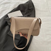 A beige vintage curved flap shoulder bag is held by a hand against a gray blazer.