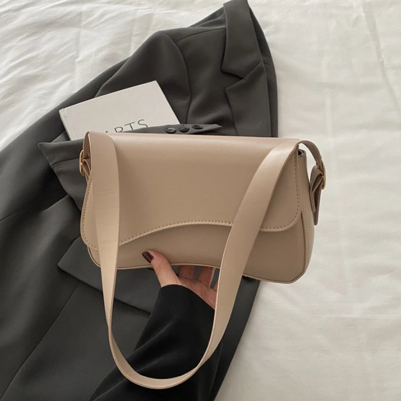 A beige vintage curved flap shoulder bag is held by a hand against a gray blazer.
