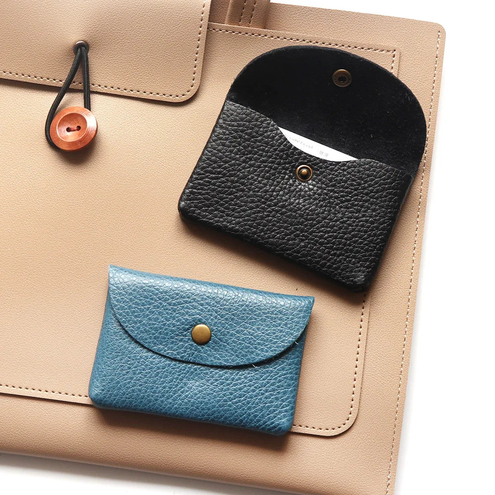 A beige leather card holder with a black flap and a teal blue leather coin purse resting on the surface.