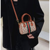 A woman holds an elegant leather tote diaper bag with a crossbody strap under a black blazer.