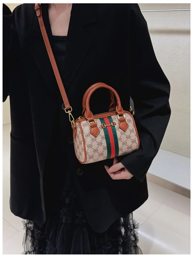 A woman holds an elegant leather tote diaper bag with a crossbody strap under a black blazer.