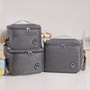 A gray insulated lunch tote bag with a handle and adjustable strap is shown on a white surface.