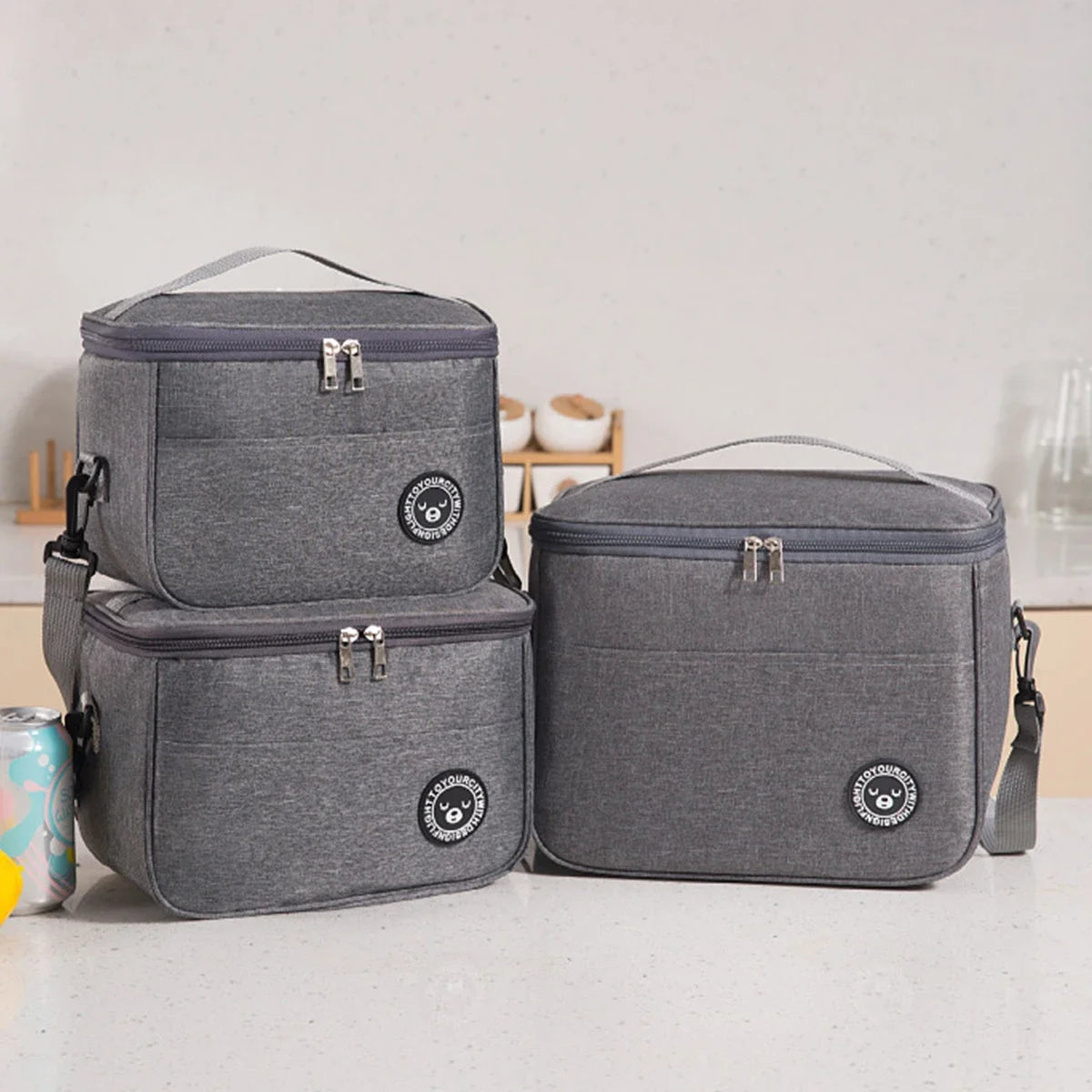 A gray insulated lunch tote bag with a handle and adjustable strap is shown on a white surface.