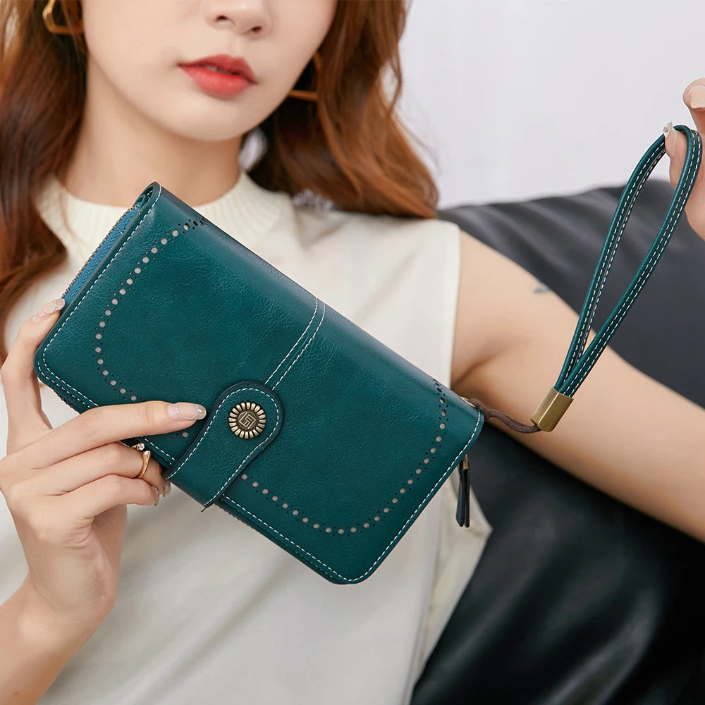 A close-up of a dark teal RFID anti-theft multi-card wallet with a leather wrist strap being held by a woman.
