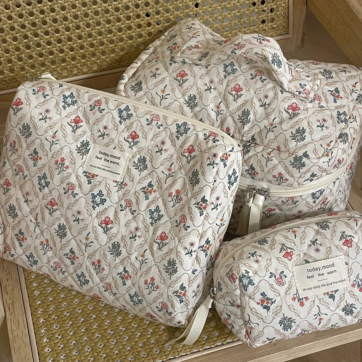 A set of quilted cotton makeup organizers in a floral pattern are displayed on a wooden surface.