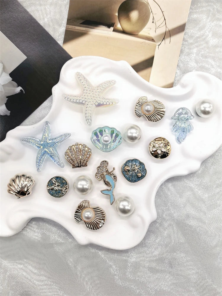 A collection of golden and iridescent sea-themed shoe charms including starfish, conches, and pearls displayed on a white sur
