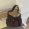 A dark brown plaid nylon drawstring tote bag resting on a wooden surface next to a white wall.