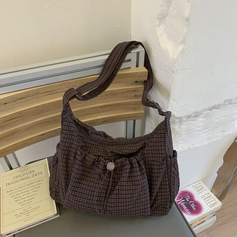 A dark brown plaid nylon drawstring tote bag resting on a wooden surface next to a white wall.