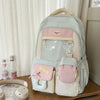 A light green Kawaii Harajuku backpack with a pink laptop compartment and accessories is displayed on a wooden surface.