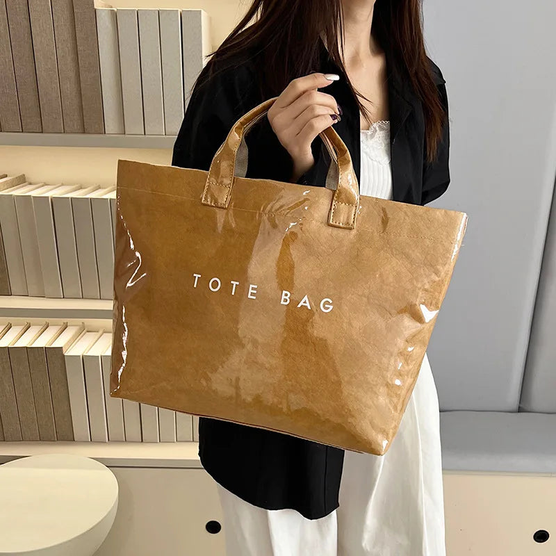 A woman holds a brown transparent waterproof PVC tote bag in front of light-colored shelving.