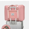 A pink canvas travel storage bag is shown resting on top of a silver suitcase.
