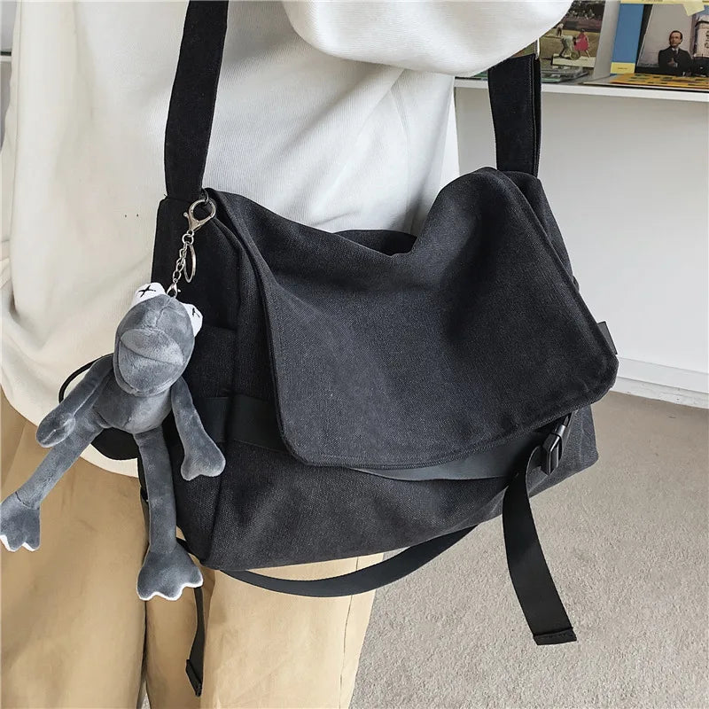 Una mujer sostiene un bolso cruz de lona negra con un dije de peluche gris.