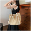 A woman holds a straw woven tote bag with PU trim and matching pouch against a wooden cabinet.
