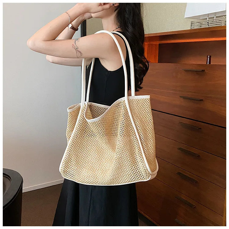 A woman holds a straw woven tote bag with PU trim and matching pouch against a wooden cabinet.