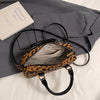 Leopardenmuster-Designer-Hobo-Tasche mit goldfarbener Hardware, vor grauem Stoffhintergrund.