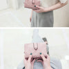A woman holds a pink frosted card wallet with a silver strap in a light indoor setting.