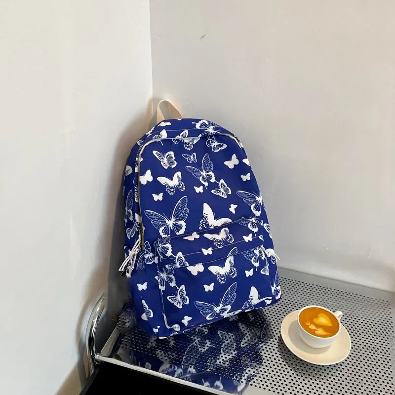 A blue backpack patterned with white butterflies resting on a gray surface.