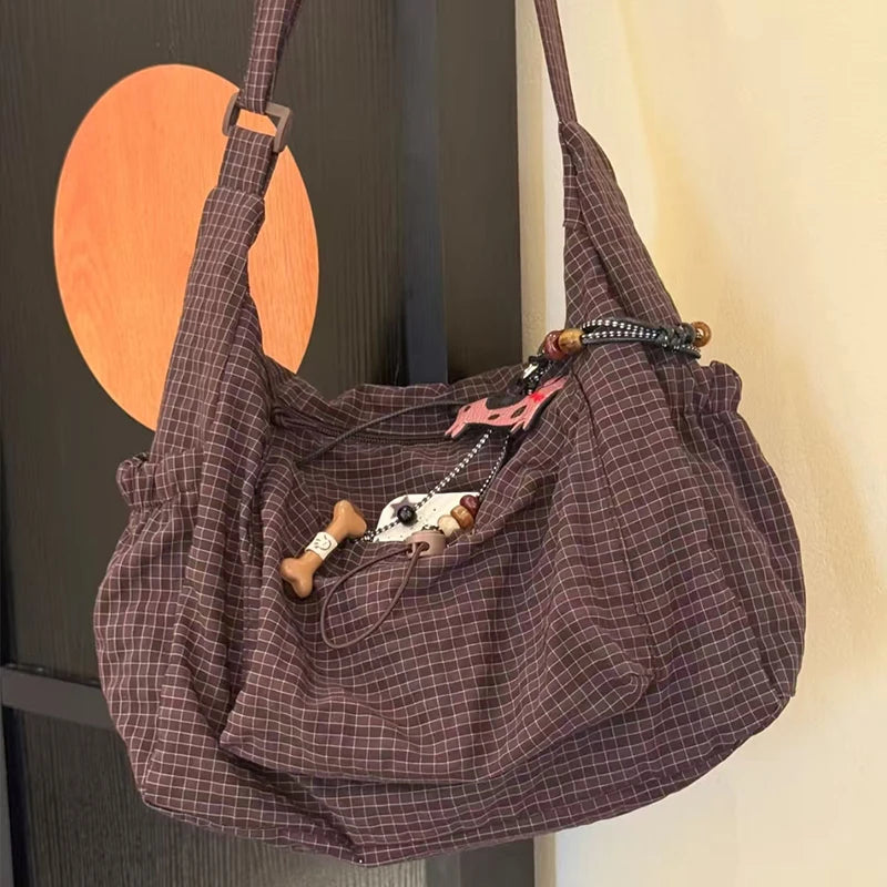 A plaid nylon drawstring tote bag hanging against a dark background.