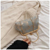 A light blue embroidered silk evening clutch with a gold chain strap resting on a beige fabric.