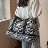 A white and black zebra-striped nylon travel duffle bag carried by a person.