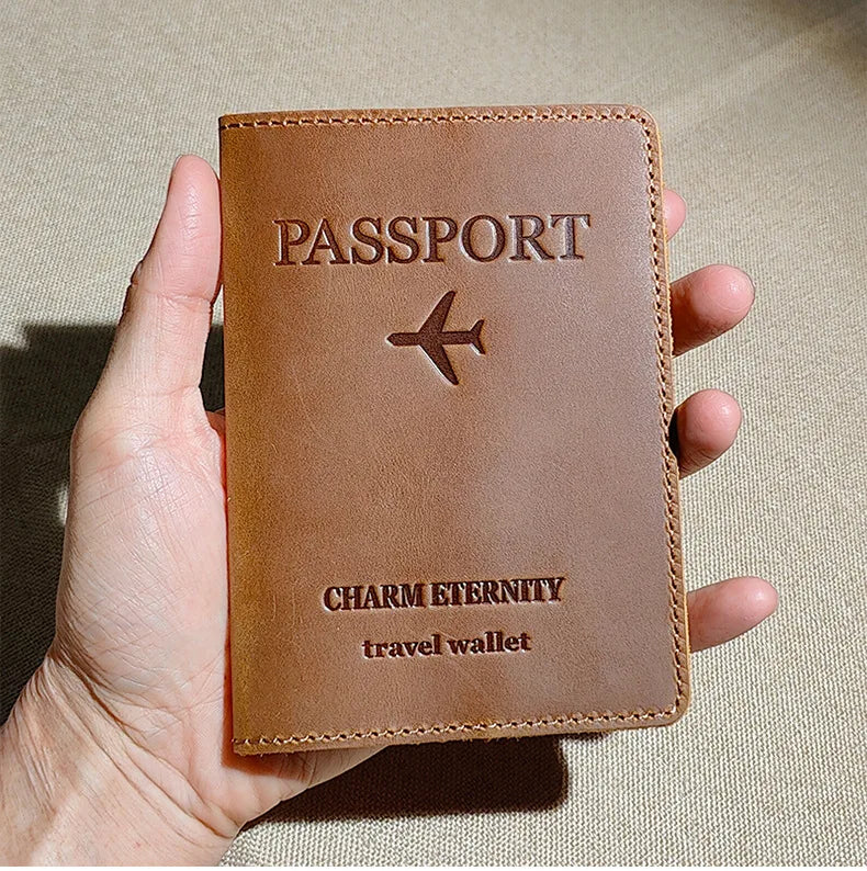 A brown leather passport holder with a stitched design and a small airplane emblem is held in a hand.
