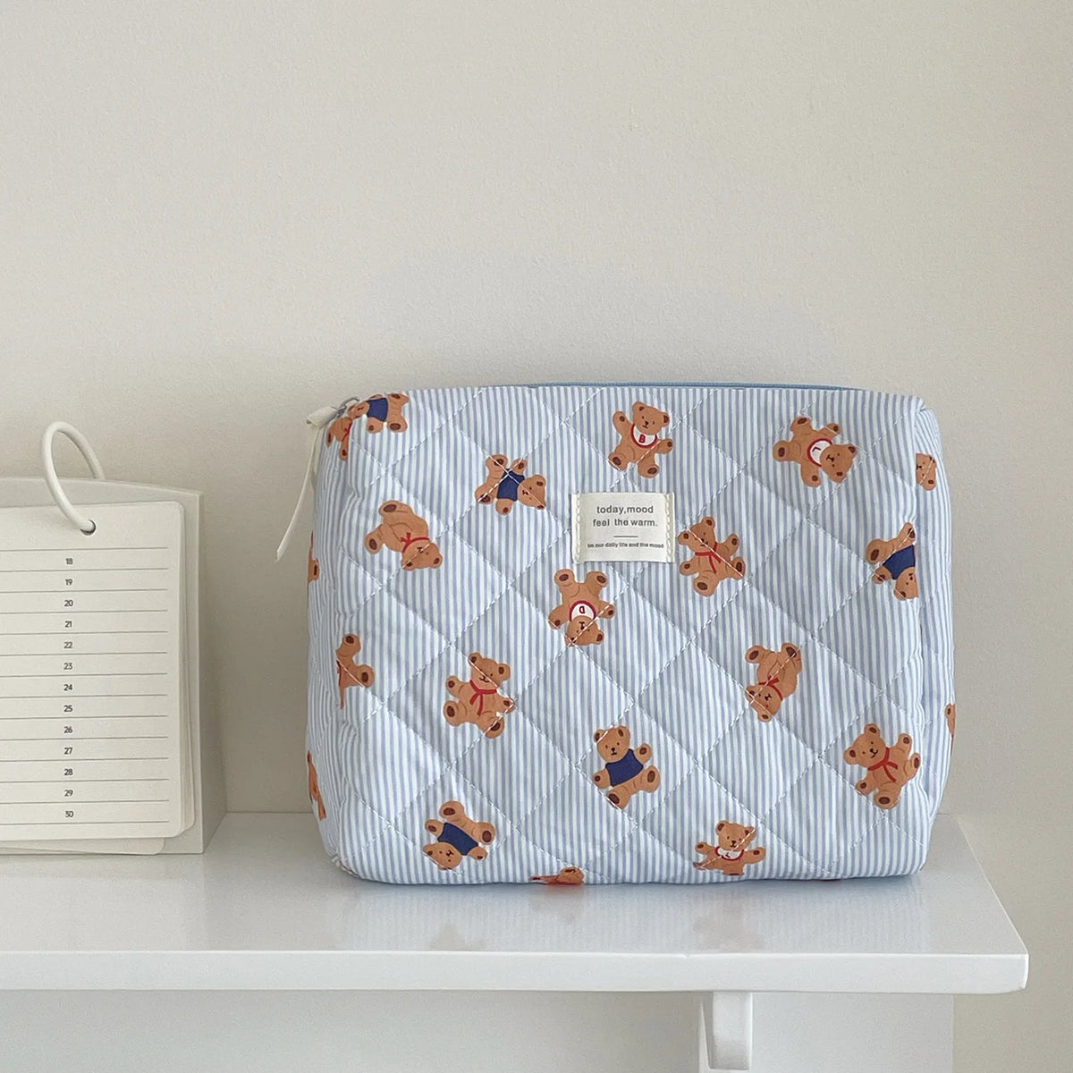 A light blue striped cosmetic makeup bag featuring a pattern of small, tan teddy bears.