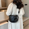 A woman wearing a white coat holds a black leather crossbody bag with a silver chain and adjustable strap.