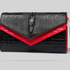 Black alligator pattern leather clutch bag with a red accent and gold chain.