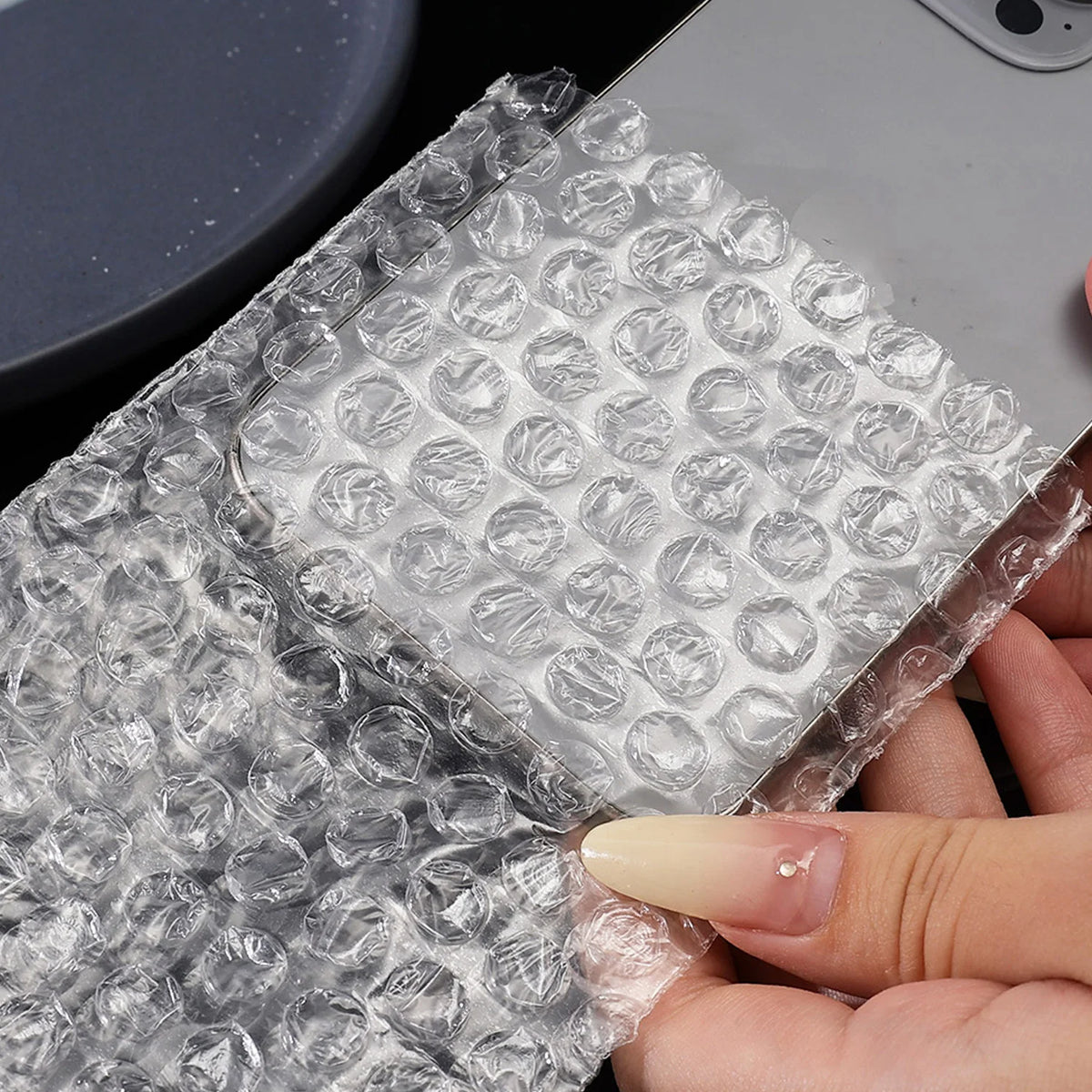 A hand holds a clear self-sealing bubble mailer bag filled with protective cushioning.
