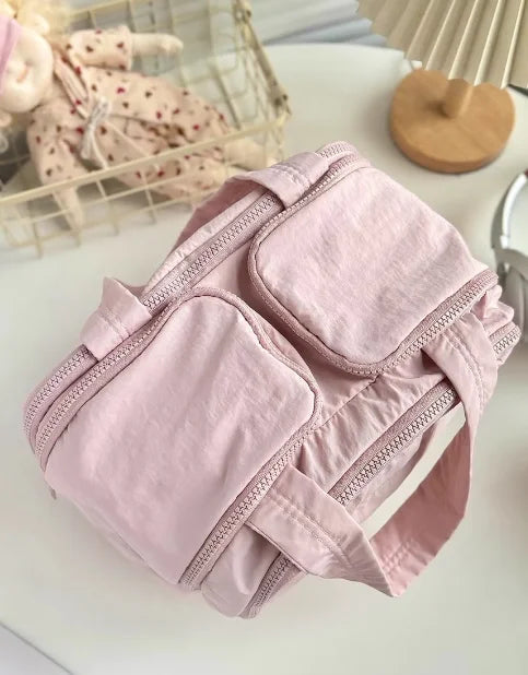 A light pink multipocket travel toiletry bag with zipper details is shown on a white surface.