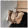 A beige canvas shoulder tote bag is displayed hanging on a dark jacket next to a window blind.