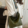 A close-up of a green leather shoulder bag with a wide patterned strap being held by a person in a white coat.