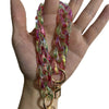 A hand holds a colorful resin chain strap with pink and green hues and a gold charm.