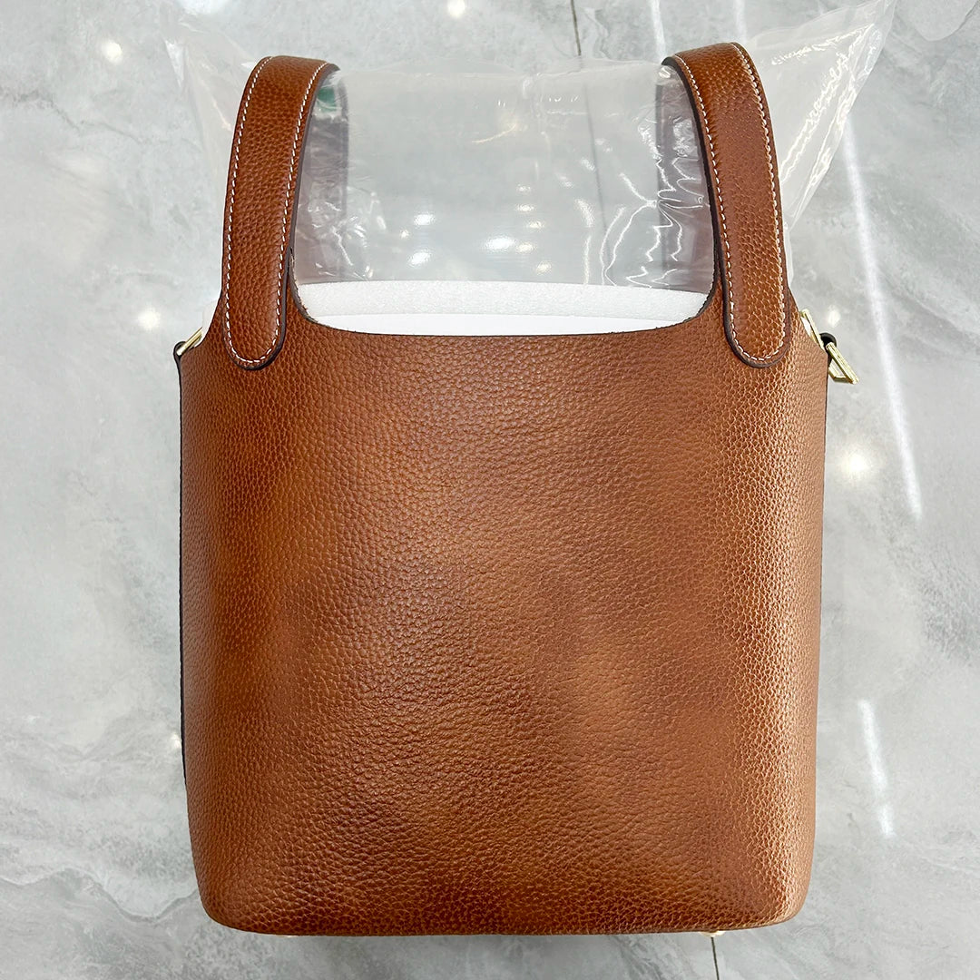 A brown genuine leather bucket bag is displayed inside clear plastic packaging.