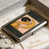 An Art Deco metal card case featuring a stylized illustration of two faces embracing on a pink background.