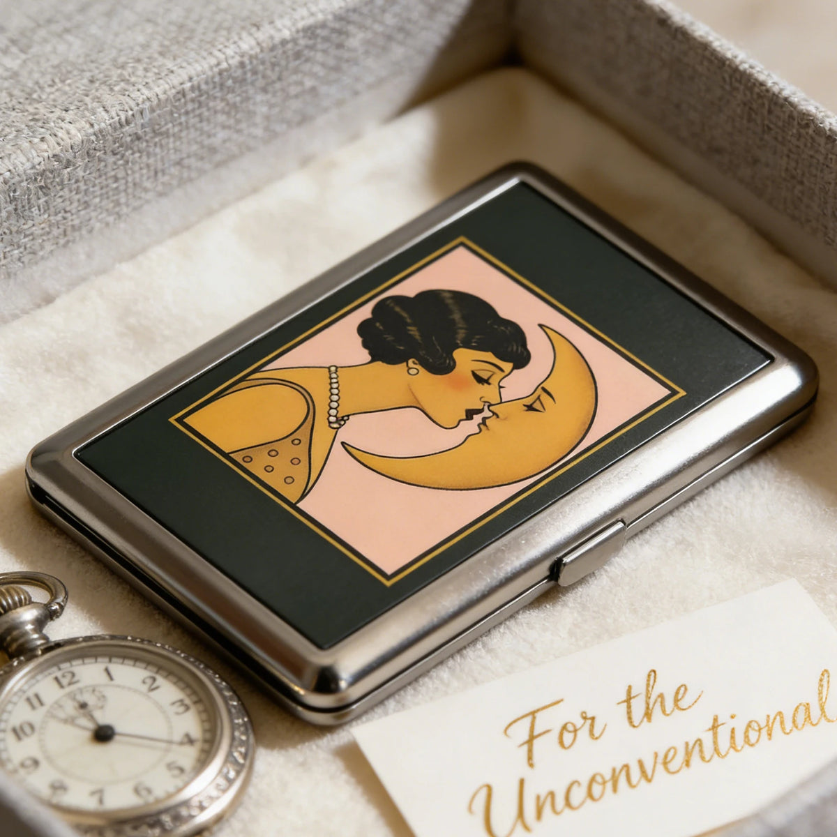 An Art Deco metal card case featuring a stylized illustration of two faces embracing on a pink background.