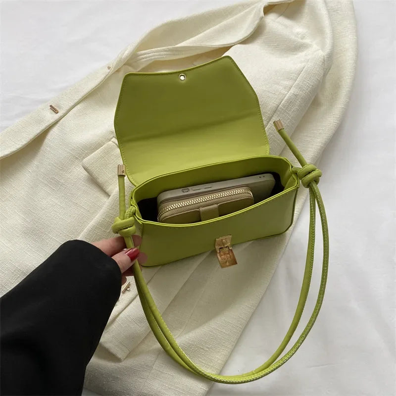 A lime green leather crossbody bag with a flap is shown open, resting on a cream-colored fabric.