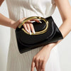 A woman holds a black clutch purse with a gold handle against a white ribbed dress.
