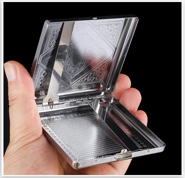 A hand holds open a decorative metal cigarette storage box showing intricate patterns on the lid and perforated bottom.