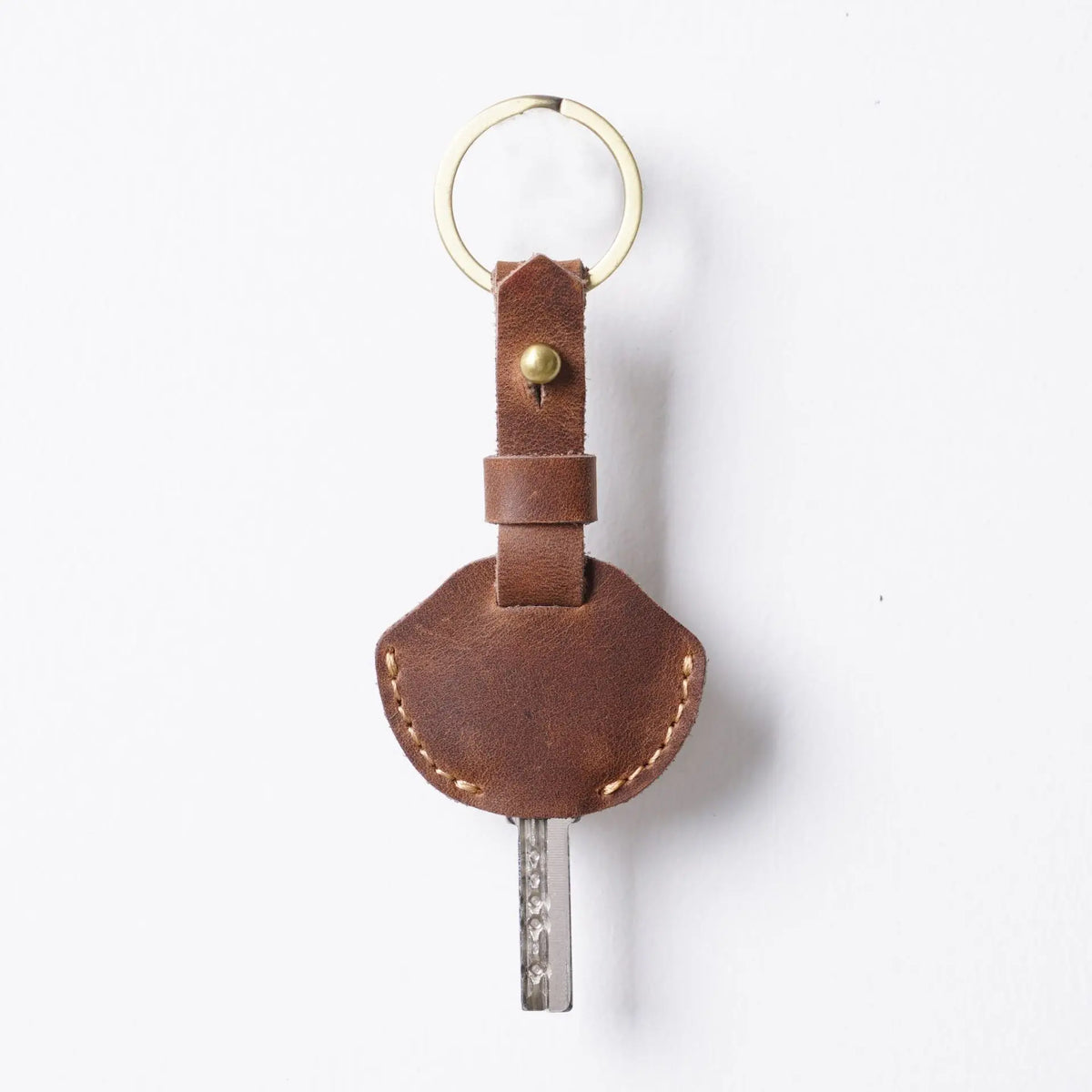 A brown genuine leather key fob cover with a metal keychain ring and key.