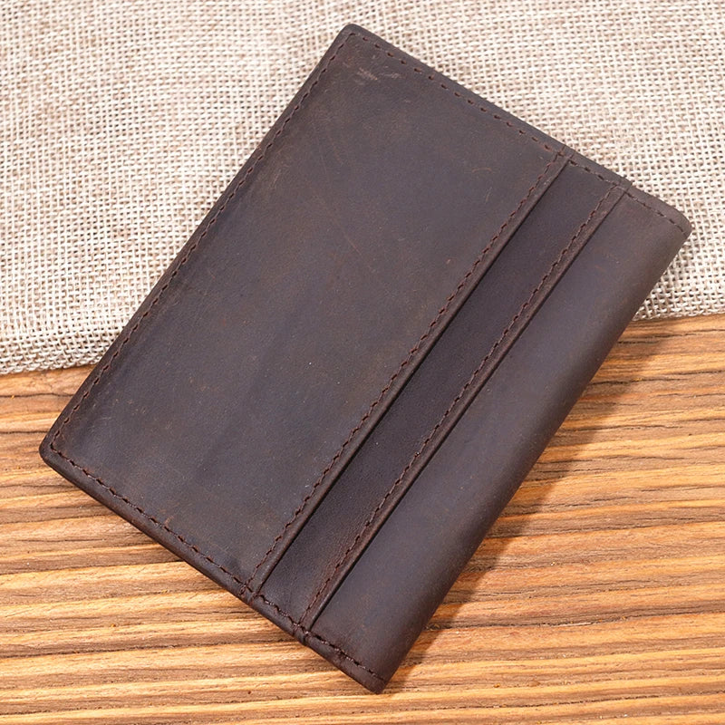 A dark brown genuine leather bifold card holder resting on a wooden surface.