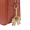 Gold-toned leopard print bow and heart bag charm keychain attached to a brown leather handbag.