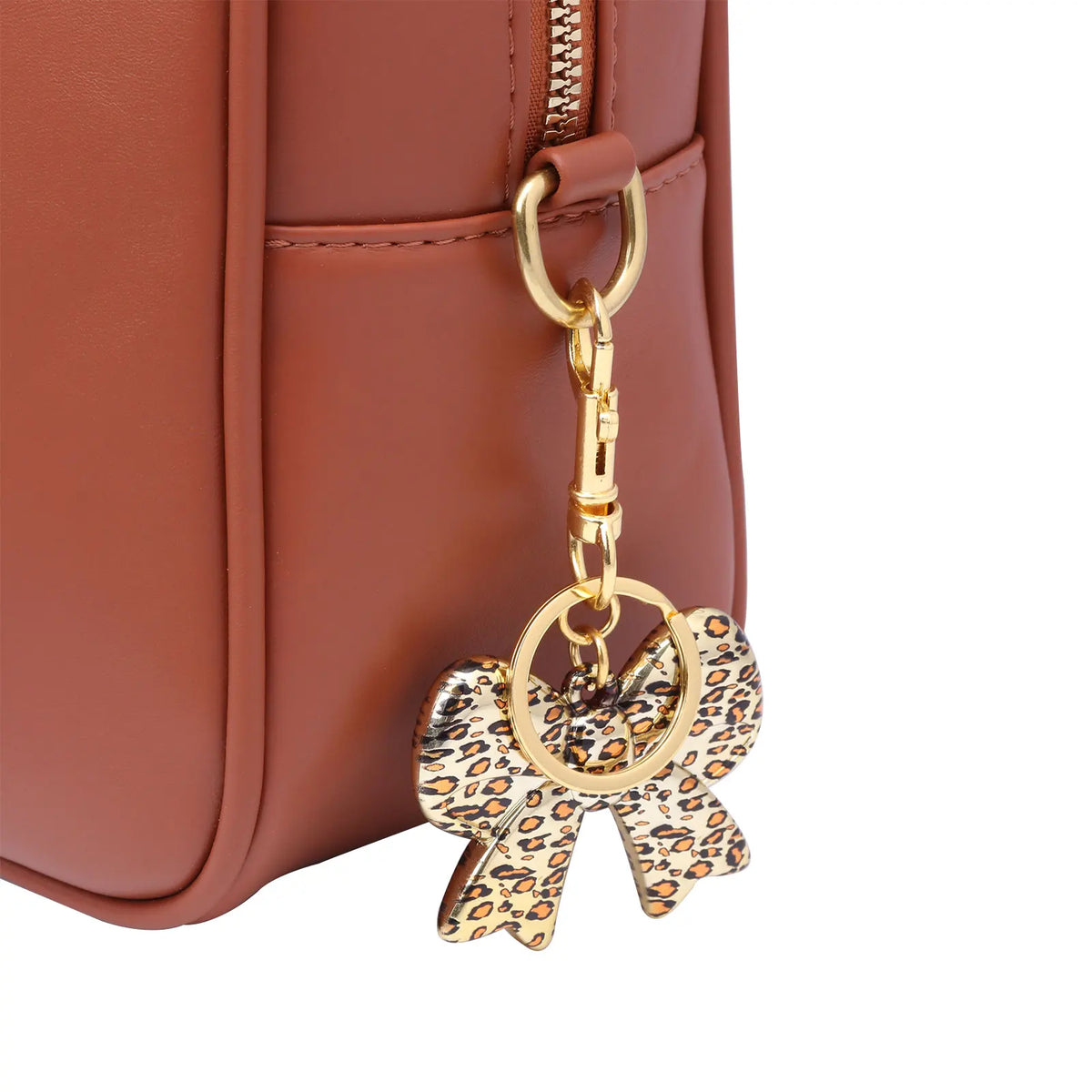 Gold-toned leopard print bow and heart bag charm keychain attached to a brown leather handbag.