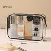 A clear plastic toiletry bag with a black zipper holds several glass bottles and tubes of skincare products.