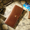 A brown genuine leather long bi-fold wallet with a snap closure resting on aged paper.